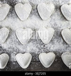 Ravioli kochen. Herzförmige Klöße, Mehl und Nudel auf hölzernem Hintergrund. Draufsicht Stockfoto
