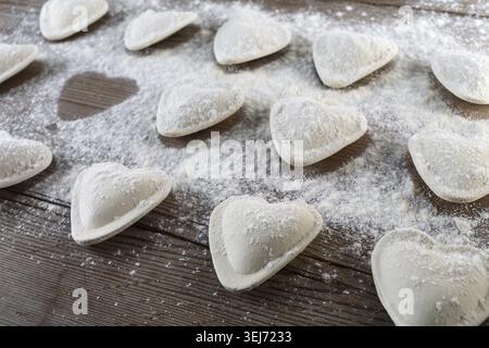 Rohe Ravioli in Form von Herzen, mit Mehl bestreuen, auf dunklem hölzernem Hintergrund. Kochenknödel. Geringe Schärfentiefe Stockfoto