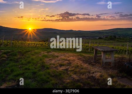 Goldener Sonnenaufgang über Vineyard Hills in ruhiger Landschaft mit rustikalem Tisch im Vordergrund und Lens Flare on the Image Stockfoto