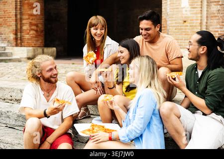 Freunde, die auf Treppen sitzen und Pizza in Italien teilen Stockfoto