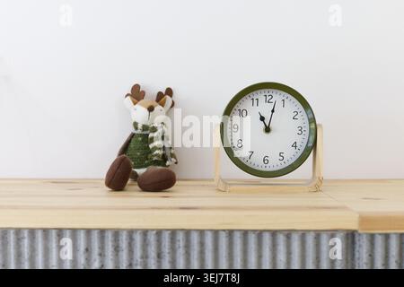 Niedliches Plüschtier-Hirsch in grünem Pullover und Schal und schlichter, grüner Uhr auf der Holztheke Stockfoto