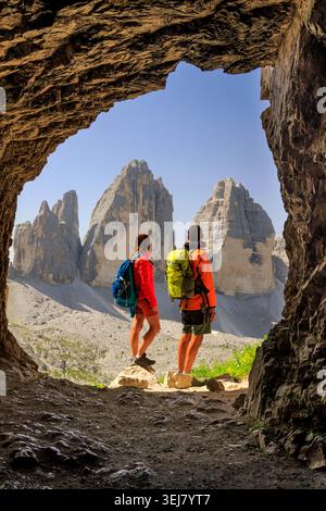 Zwei Wanderer bewundern die berühmte Tre Cime di Lavaredo durch einen natürlichen Felsbogen in den Dolomiten. Stockfoto