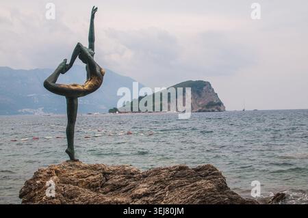 Eine anmutige Bronzeskulptur eines Tänzers sitzt auf einer Klippe mit Blick auf die Adria und die Insel St. Nikolaus in Budva, Montenegro Stockfoto