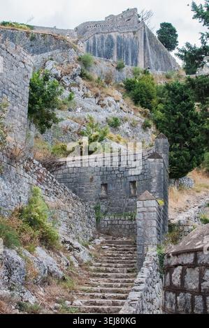 Niedrigwinkelaufnahme der historischen Steinmauern der Festung St. John und Stufen, die sich auf einen felsigen Berghang in Montenegro schlängeln. Stockfoto