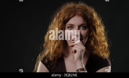 Eine Frau fühlt sich nervös und unsicher, beißt sich in die Fingernägel mit rotem lockigem Haar Stockfoto