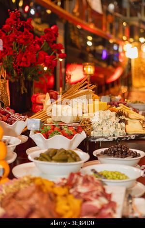 Ein Bankettaufstrich mit verschiedenen Käsesorten, Brotstäbchen, Erdbeeren, Oliven und Obst, das elegant für eine Abendveranstaltung arrangiert wird Stockfoto