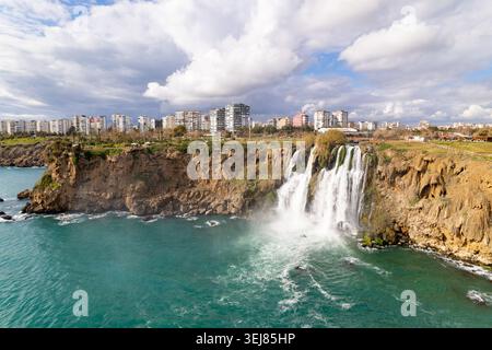 Mächtige Bäche des Düden Wasserfalls stürzen durch zerklüftete Küstenklippen in das türkisfarbene Mittelmeer, umgeben von üppigen natürlichen Texturen. Stockfoto