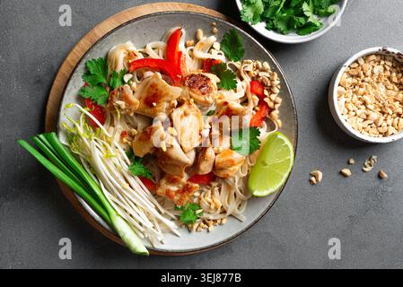 Authentische Thai Chicken Pad Thai Nudeln mit gemahlenen Erdnüssen, Sojasprossen, Koriander und Limette. Thailändische Mahlzeit, gebratene Hühnernudeln auf Beton rühren Stockfoto