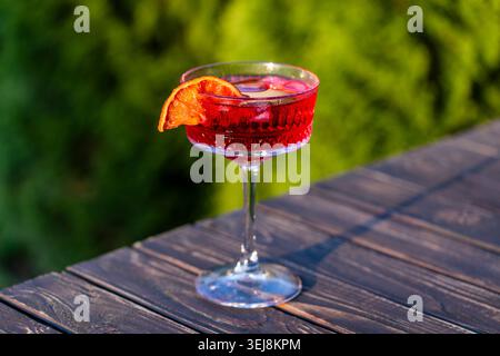 Roter Sommercocktail garniert mit getrockneter Orangenscheibe. Ein Kristall-Coupé-Glas, gefüllt mit einem leuchtenden roten alkoholischen Cocktail und Eiswürfeln, steht auf einem Stockfoto