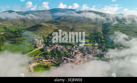 Bergdorf in Katalonien umgeben von Morgennebel und grünen Hügeln, aus der Vogelperspektive auf die ländliche Landschaft in der Nähe der Pyrenäen in Spanien Stockfoto