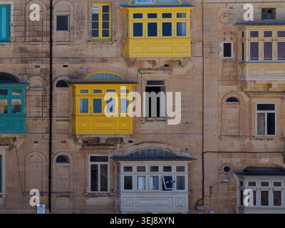 Helle Fenster heben sich von traditionellen Steinhäusern in Valletta, Malta, ab. Die Szene fängt die einzigartige Architektur entlang einer Stadtstraße ein. Stockfoto