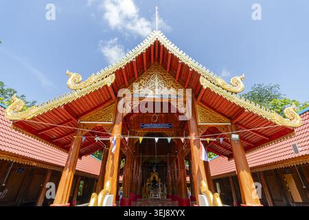 Dok Kham Tai, Phayao, Thailand - 28. Mai 2026: Wat Chaloem Phra Kiat (Wat San Pa Fang), gestufter Holzgiebel mit goldenen Naga-Finials und Buddha-Statue. Stockfoto