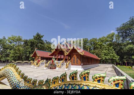 Dok Kham Tai, Phayao, Thailand - 28. Mai 2026: Wat Chaloem Phra Kiat (Wat San Pa Fang), Holzsaal mit Nagatreppen und Bäumen. Stockfoto