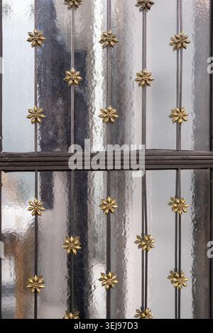 Ein kunstvoll verziertes schmiedeeisernes Sicherheitsgitter mit goldfarbenen Blumenakzenten, das ein Milchglasfenster bedeckt, ist an der Außenfassade des Gebäudes angebracht. Stockfoto