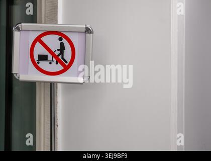 Ein Metallwarnschild mit einer durchgestrichenen Figur mit einem Handwagen steht an einem Innenkorridor des Gebäudes. Stockfoto