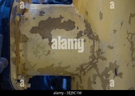 Nahaufnahme einer dicken Metallleitung mit stark abblätternder gelber Farbe in einem Innenbetrieb Stockfoto