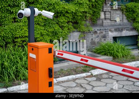 Orangefarbenes automatisches Parksperrtor mit eingebauten Sicherheitskameras verhindert den Zugang zu einer Zufahrt im Freien. Stockfoto