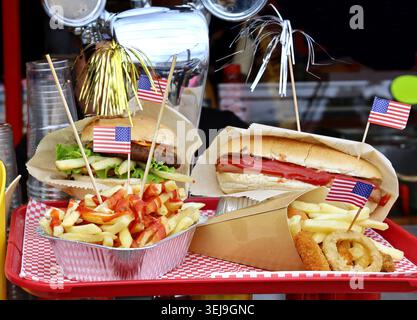 Amerikanische Fast-Food-Spezialitäten. Pommes Frites und Zwiebelringe vorne und Burger und Hot Dog hinten. Jedes Gericht hat eine US-Flagge Stockfoto