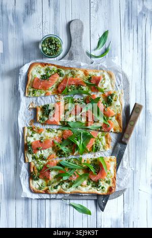 Rustikale Fotos von einem frisch gebackenen Flamkuchen mit Räucherlachs, wilden Knoblauchblättern und cremigem Käse. Das Fladenbrot ruht auf Parchm Stockfoto