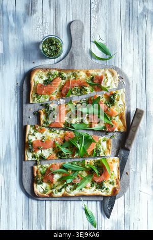 Rustikale Fotos von einem frisch gebackenen Flamkuchen mit Räucherlachs, wilden Knoblauchblättern und cremigem Käse. Das Fladenbrot ruht auf Parchm Stockfoto
