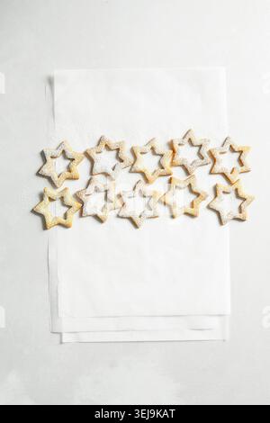 Minimalistische Komposition aus sternförmigen Spitzbuben, die mit Puderzucker bestäubt und ordentlich auf weißem Pergamentpapier angeordnet sind. Th Stockfoto