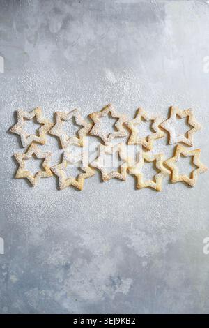 Minimalistische Komposition aus sternförmigen Spitzbuben, die mit Puderzucker bestäubt und ordentlich auf weißem Pergamentpapier angeordnet sind. Th Stockfoto