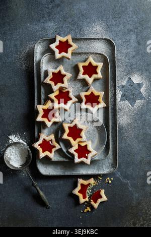 Blick von oben auf sternförmige Spitzbuben gefüllt mit hellroter Marmelade und mit Puderzucker bestäubt. Die Kekse sind auf einem Metalltris angeordnet Stockfoto