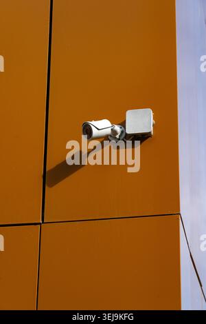 Überwachungskamera auf orangefarbenem Gestell, die moderne Sicherheitsmaßnahmen in zeitgenössischer Architektur hervorhebt Stockfoto