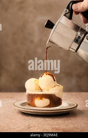 Vertikal Shot oder affogato al Caffe, typisch italienisches Dessert, häufig als Ende der Mahlzeit, jemand hält eine Espressomaschine und gießt Kaffee über das i Stockfoto