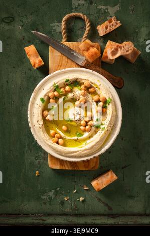 Flacher, hausgemachter Hummus-Dip auf grünem Hintergrund, mit frischen Kichererbsen und Petersilie, Olivenöl und Pitabrot gestylt Stockfoto