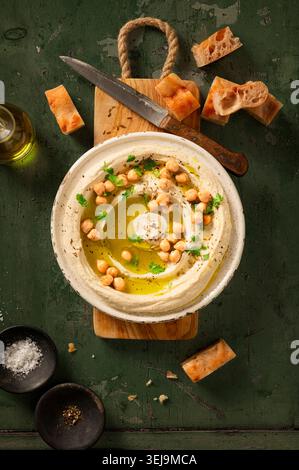 Flacher, hausgemachter Hummus-Dip auf grünem Hintergrund, mit frischen Kichererbsen und Petersilie, Olivenöl und Pitabrot gestylt Stockfoto