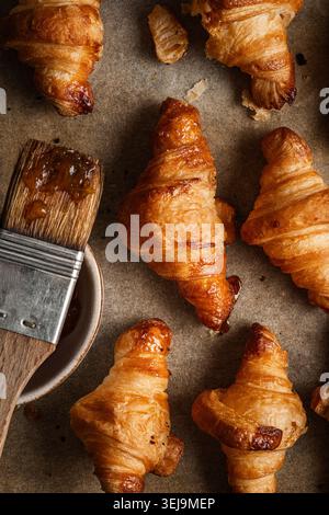 Tablett mit frisch gebackenen goldenen Croissants, auf Backpapier angeordnet. Das warme Licht unterstreicht die goldenen Farbtöne und die knusprige Textur des Teigs cre Stockfoto