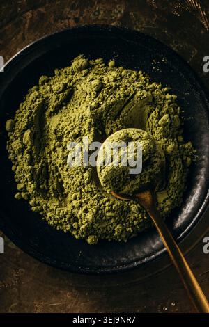 Nahaufnahme von Matcha-Pulver auf einer schwarzen Platte mit einem goldenen Löffel Stockfoto