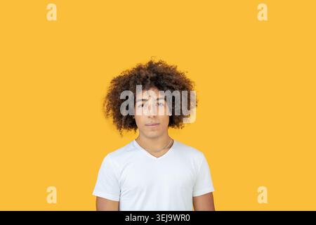 Portrait schöne Männer gemischter Rasse auf gelbem Hintergrund. Ein junger ethnischer Mann mit lockigen Haaren in einem weißen T-Shirt sieht entspannt aus. Wunderschön jung Stockfoto