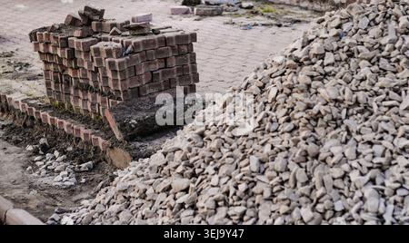 Stapel von Pflasterziegeln neben einem Schotterhaufen bei der Umgestaltung des Gehwegs, die Baumaterialien und städtische Sanierungsarbeiten zeigen. Stockfoto