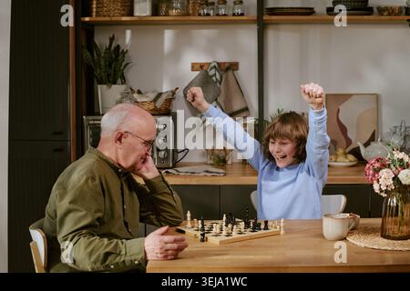 Seniorenmann spielt Schach mit Kind und feiert den Sieg zu Hause Stockfoto