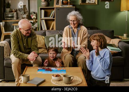 Seniorenpaar und Kinder spielen zusammen Puzzle zu Hause Stockfoto