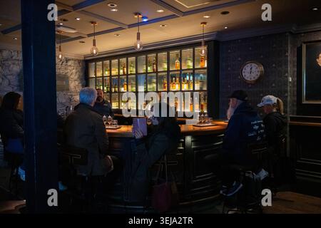 Dublin Irland - 11. Oktober 24: Innenansicht der Bar in der Jameson Distillery Bow St mit Besuchern am Schalter und hinterleuchteten Whiskey-Flaschen auf d Stockfoto