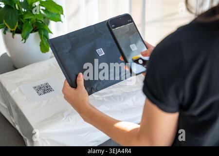Smartphone scannt kleinen QR-Code auf dem Paket mit Fokus auf dem Etikett für die Nachverfolgung der Zustellung zu Hause. Kontaktlose Identifizierungs- und Logistiktechnologie Stockfoto