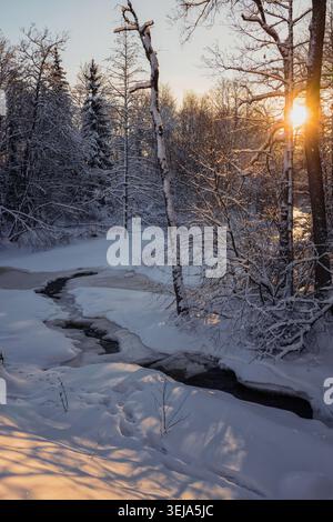 Gumböle, Finnland - 2024-01-06: Eine wunderschöne Winterlandschaft mit einem sich windenden Bach, der teilweise von Schnee und Eis bedeckt ist und von schneebedeckten Tre umgeben ist Stockfoto