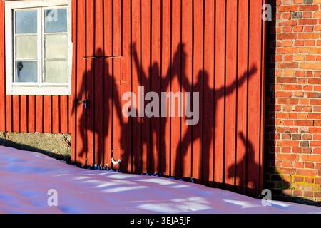 Gumböle, Finnland - 06.01.2024: Die Silhouetten von Menschen mit erhobenen Armen werden wie Schatten auf eine hellrote Holzwand in Gumböle, Espoo, Finnland geworfen Stockfoto