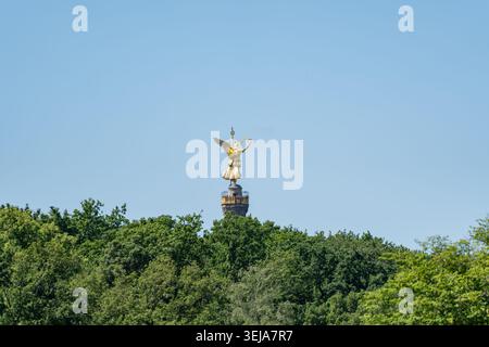 Die goldene Victoria-Statue steht hinter einem breiten Laubdach in Berlin. Die minimalistische Komposition lässt den blauen Himmel über dem Histori offen Stockfoto