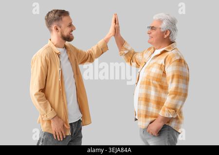 Senior-Mann und sein Sohn geben einander High-Five auf grauem Hintergrund Stockfoto