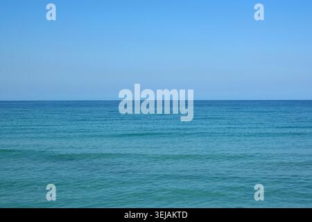 Weitläufige Meereslandschaft mit klarem blauem Himmel und türkisfarbenem Wasser, die einen ruhigen Horizont schaffen. Stockfoto