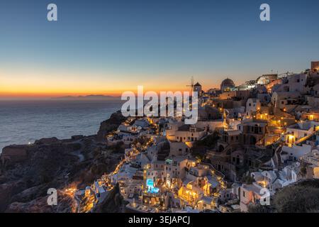 Wunderschöner Sonnenuntergang Blick auf beleuchtete weiße Häuser und Windmühlen auf der Klippe des Dorfes Oia in Santorin, Griechenland, über der Ägäis Stockfoto