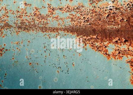 Grunge-Hintergrund eines rostigen Metallblechs mit Resten von abblätternder türkisfarbener Farbe. Starke Korrosion, orangene Roststruktur und verwitterte Optik. Stockfoto