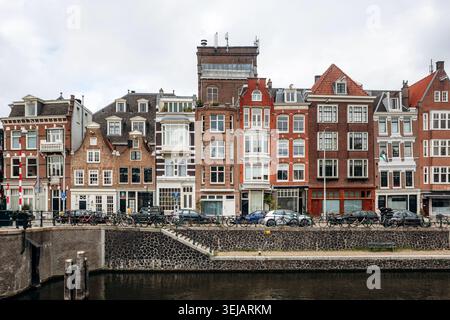 Amsterdam, Niederlande - 18. April 2026: Reihe traditioneller Kanalhäuser entlang der Uferpromenade von Amsterdam, mit historischer niederländischer Architektur und Stockfoto
