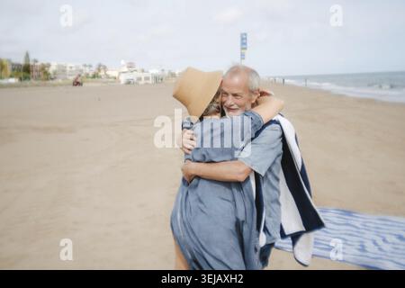 Seniorenpaar, das sich an einem Sandstrand umgibt, lächelt und einen liebevollen Moment während ihres entspannten Urlaubs genießt, symbolisiert dauerhafte Liebe und glückliche Ruhe Stockfoto