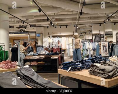 PFORZHEIM, DEUTSCHLAND - 28. MAI 2026 Innenansicht einer modernen Bekleidungsboutique mit gefalteten Jeans auf Präsentationstischen, Schaufensterpuppen, Kleiderbügeln mit Kleidung und Stockfoto