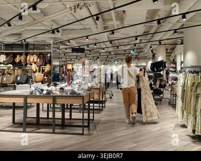 PFORZHEIM, DEUTSCHLAND - 28. MAI 2026 Frau, die Kleidung auswählt und Kleidung hält, während sie in einem modernen Bekleidungsgeschäft mit Kleiderbügeln und Di einkaufen Stockfoto